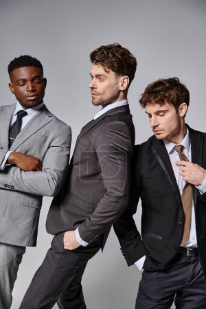 young attractive multicultural men in business smart suits posing together on gray background