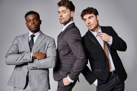 Téléchargez les photos : Jeunes beaux hommes multiculturels en affaires costumes intelligents posant ensemble sur fond gris - en image libre de droit
