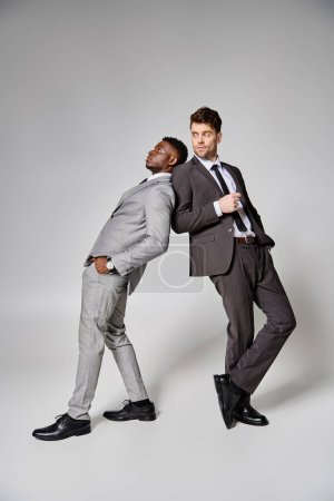 deux attrayants modèles masculins multiculturels élégants en affaires vêtements intelligents posant sur fond gris