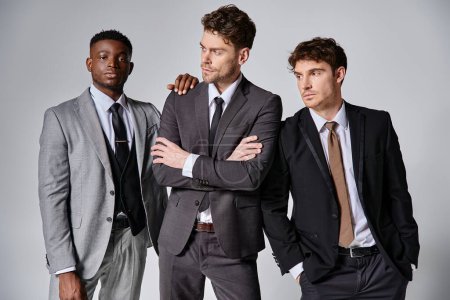 attractive young interracial friends in smart business suits posing together on gray background