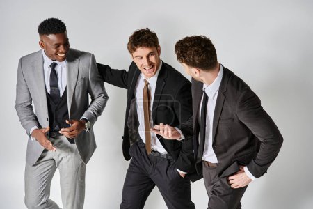Téléchargez les photos : Jeunes amis multiculturels heureux en affaires tenues élégantes souriant joyeusement sur fond gris - en image libre de droit