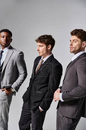 Téléchargez les photos : Attrayants modèles masculins multiculturels élégants en affaires élégants costumes intelligents posant sur fond gris - en image libre de droit