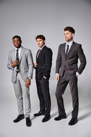 Téléchargez les photos : Attrayant modèles masculins multiculturels élégants en affaires élégants costumes intelligents posant sur fond gris - en image libre de droit