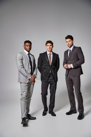 Téléchargez les photos : Beaux modèles masculins multiculturels en affaires élégants costumes intelligents posant sur fond gris - en image libre de droit