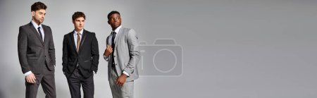Téléchargez les photos : Attrayants modèles masculins interracial en affaires élégants costumes intelligents posant sur fond gris, bannière - en image libre de droit