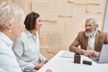 Photo for Middle aged multicultural lgbt couple sitting next to bearded realtor in real estate office - Royalty Free Image