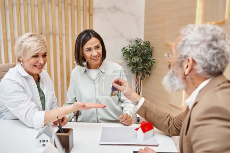 middle aged realtor giving house key to happy interracial lgbt couple in real estate office