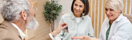 Photo for Middle aged realtor giving house key to happy interracial lgbt couple in real estate office, banner - Royalty Free Image