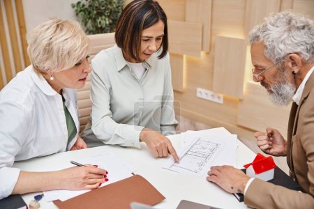 Photo for Realtor showing blueprint of apartment to middle aged interracial lgbt couple in real estate office - Royalty Free Image