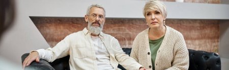 atenta pareja de mediana edad sentado en el sofá de cuero y mirando psicólogo, pancarta