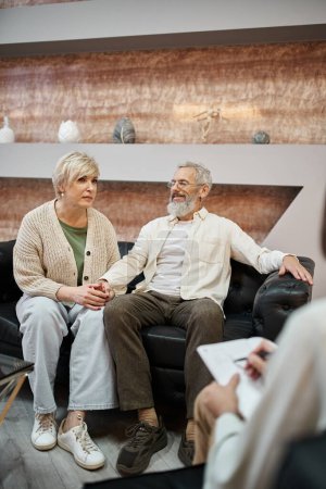 Ehepaar mittleren Alters sitzt auf Ledercouch in der Nähe von Psychologen und macht sich Notizen während der Beratung