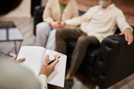 Psychologe hält während Familienberatung Stift und Notizbuch in der Nähe von Eheleuten