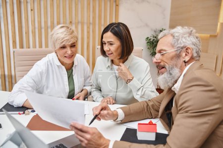 middle aged bearded realtor showing contract to lgbt family in real estate office, lesbian couple