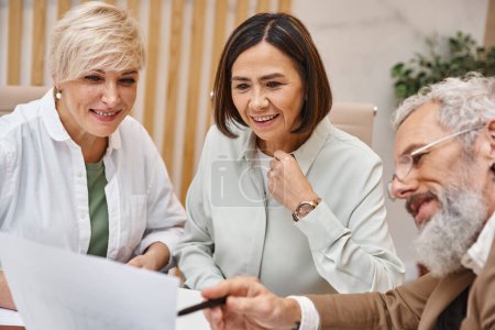 Photo for Middle aged bearded realtor showing contract to lesbian couple in real estate office, lgbt couple - Royalty Free Image