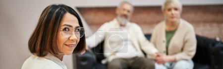 Photo for Banner, middle aged psychologist in glasses looking at camera near married couple on backdrop - Royalty Free Image