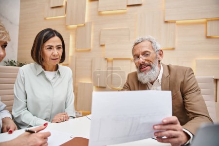 bearded realtor showing contract to lesbian couple in real estate office, middle aged lgbt family