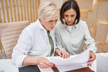 pareja lesbiana de mediana edad discutiendo la compra de bienes raíces y mirando el contrato