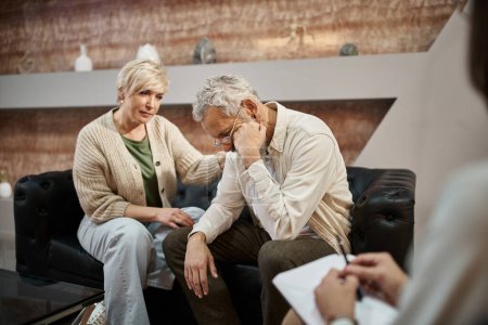 caring middle aged wife calming upset husband during family therapy session with psychologist