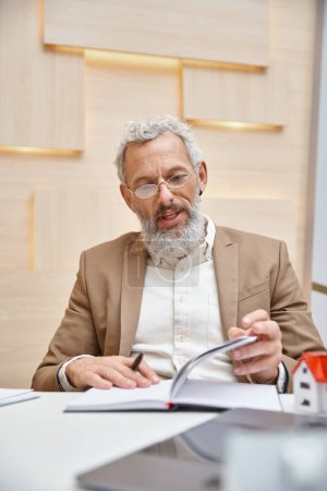 middle aged real estate agent in glasses talking during consultation, checking his notes in office
