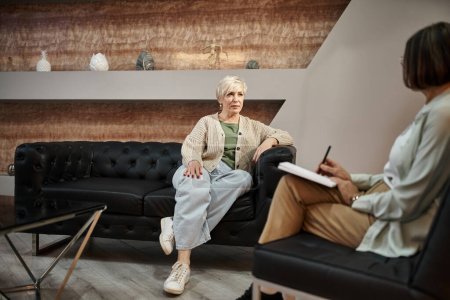 Fokus auf mittelalte blonde Frau, die auf der Couch sitzt und während der Sitzung mit einem Psychologen spricht