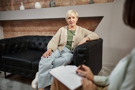 focus on middled aged woman sitting on couch and talking to female psychologist during session