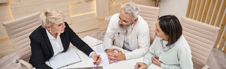 middle aged female realtor discussing project of new house with married couple in office, banner