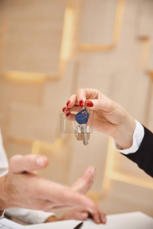 geschlossene Aufnahme eines beschnittenen Maklers, der dem Kunden im Immobilienbüro den Schlüssel vom neuen Haus übergibt