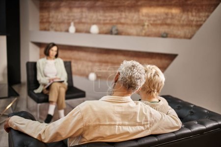 back view of married couple sitting together on sofa during therapy session with psychologist