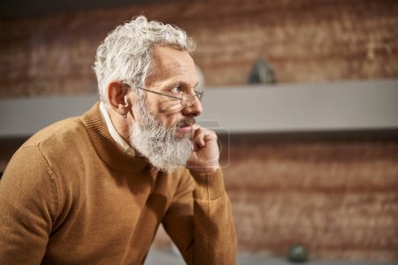 bearded middle aged psychologist in glasses looking away and listening carefully during session