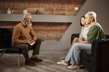 lesbian couple talking to bearded middle aged psychologist in glasses during therapy session