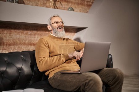 joyful middle aged psychologist with beard talking during online consultation with client on laptop