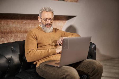 joyful middle aged psychologist with beard laughing during online consultation with client on laptop