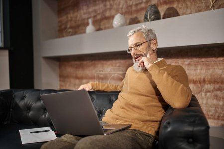 psicólogo de mediana edad con barba hablando con el cliente durante la consulta en línea en el ordenador portátil
