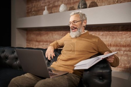 cheerful middle aged psychologist with beard talking to client during online consultation on laptop