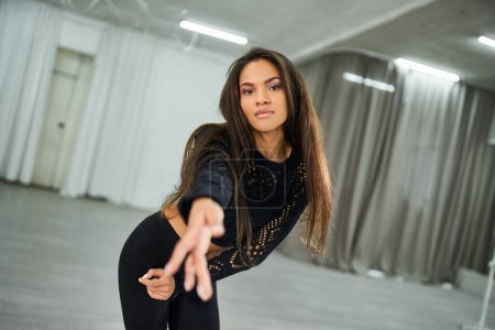 graceful long-haired african american woman looking at camera and dancing in studio, sensuality