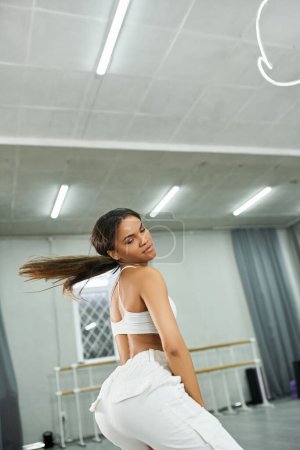 young long-haired african american dancer in white sportswear rehearsing in modern dance studio
