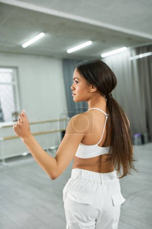 Foto de Elegante bailarina afroamericana de pelo largo en ropa deportiva blanca ensayando en un estudio de danza moderno - Imagen libre de derechos
