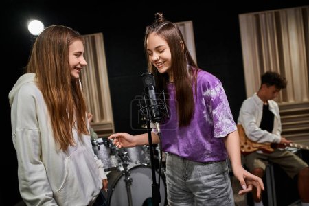 fröhliche entzückende Teenager-Mädchen, die fröhlich singen, während ihr Freund Gitarre spielt, Musikgruppe