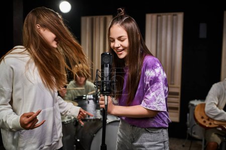 entzückende lustige Teenager-Mädchen singen und zeigen Rock-Zeichen, während Jungen verschiedene Instrumente spielen