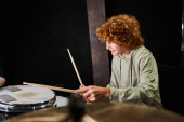 cheerful talented teenage boy with red hair in casual comfortable attire playing drums in studio Stickers #687122006