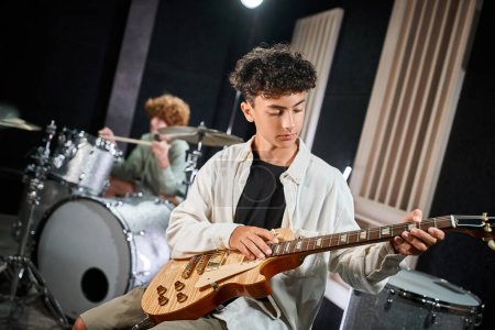 focused talented teens in casual attires playing guitar and drums in studio, musical group