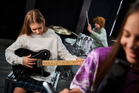 Foto de Adolescentes alegres con atuendos casuales cantando y tocando la guitarra y la batería en el estudio, grupo musical - Imagen libre de derechos