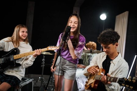 Téléchargez les photos : Joyeux adorables adolescents membres du groupe chantant et jouant divers instruments, groupe musical - en image libre de droit
