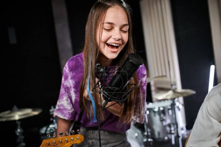 freudig entzückendes Teenager-Mädchen in lebendiger Kleidung, das im Studio aktiv ins Mikrofon singt