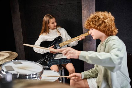 Konzentration auf konzentriertes hübsches Teenager-Mädchen, das neben ihrem verschwommenen liebenswerten Schlagzeuger Gitarre spielt
