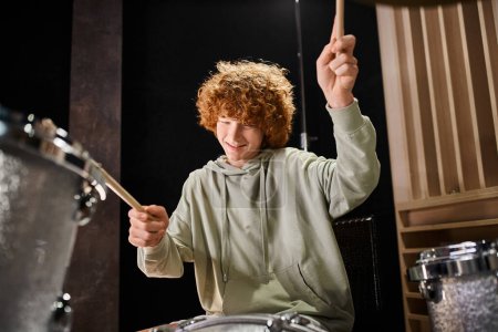 joyous talented teenage boy with red hair in everyday cozy attire playing his drums actively