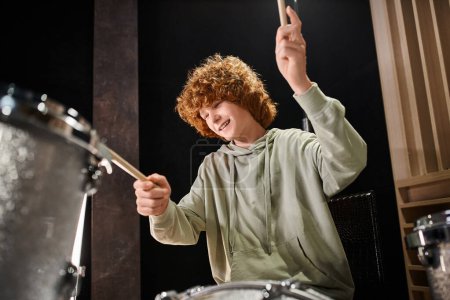 lustige talentierte rothaarige Teenager in bequemen Klamotten, die aktiv Schlagzeug spielen, während sie im Studio sind
