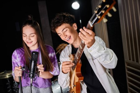 Photo for Good looking cheerful teenage boy with braces playing guitar next to his cute vocalist in studio - Royalty Free Image