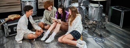 lindos adolescentes en trajes casuales sentados en el estudio escribiendo letras juntos, grupo musical, pancarta