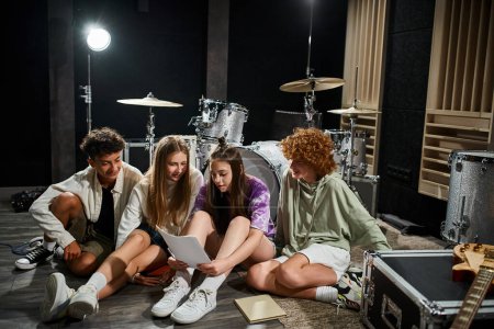 entzückende Teenager in Alltagskleidung, die im Studio sitzen und sich Texte anschauen, Musikgruppe